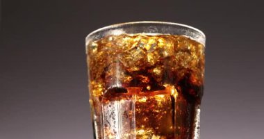 Buzlu kola bardağı yavaşça yakın çekimde dönüyor. Kahverengi arka planda dönen soğuk soda içeceği. 4K video görüntüleri