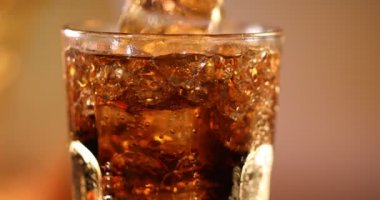 Buzlu bir bardak kola, yakın plan. Buzlu kola ve yakın planda köpüklü cam. Arka planda bulanık duran bir bardak kola. Yavaş çekim 4K video görüntüsü döndürüyor