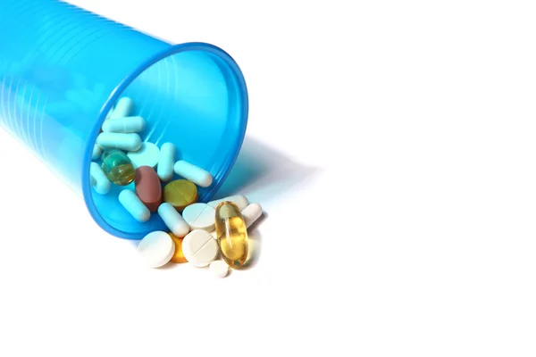 Image of different pills spilling out of a plastic glass — Stock Photo, Image