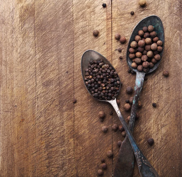 Image of spoons full of black peppercorn and allspice on wooden — Stock Photo, Image