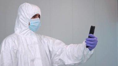 4K, PPE 'deki bir doktor İspanya' daki bir hastanede covid-19 salgını sırasında akıllı telefondaki mobil uygulamalara danışmanlık yaparken kızgın. Sağlık çalışanı teletıp konsepti. Tıp merkezinin içi.