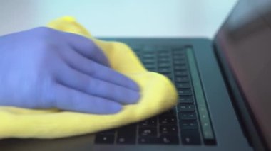 Bir sağlık görevlisi, koronavirüsün yayılmasını önlemek için laptopunu bir bezle siliyor. Bilgisayar klavyesini temizlemek ve dezenfekte etmek için eldiven takar.