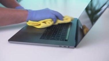 Eldiven giyen biri, koronavirüsü önlemek için dizüstünü temizler. Bir çalışma alanının dezenfeksiyon ve temizliği.