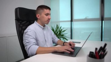 4K, beyaz adam dizüstü bilgisayar kullanıyor. Genç işçi pencerede oturuyor ve bilgisayarda akıllı telefonuyla rapor yazıyor. İş büyümesi kavramı.