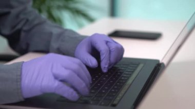 4K, koruyucu eldivenli adam bilgisayarda yazı yazıyor ve iş yerinde çoban salgını sırasında akıllı telefon kullanıyor. Ofiste genç bir ofis çalışanı. İş büyümesi ve koronavirüs kavramı.