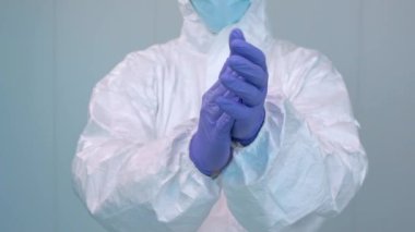 Kişisel koruma kiti içinde bir doktorun elini çırpması ve hastanenin içinde eldiven takması. Sağlık çalışanları covid-19 salgınının tedavisinin başarısını sersemletiyor.
