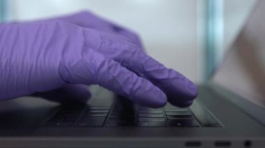 Modern dizüstü bilgisayarı olan yavaş çalışan serbest çalışan bir adam koruyucu eldiven giyer. Koronavirüs salgını sırasında bilgisayarında önemli bir şey yazıyor. İş büyümesi ve covid19 konsepti.