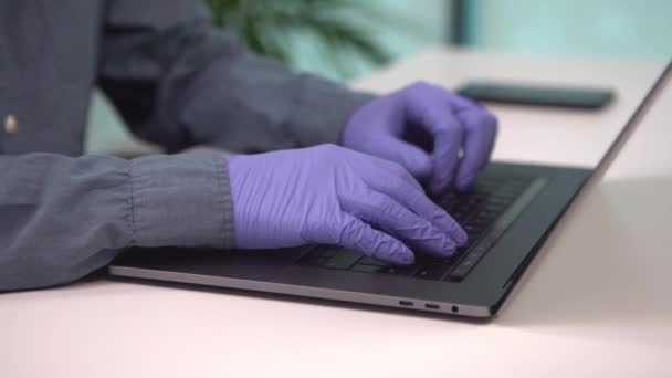 現代のラップトップを持つ若い男のフリーランサーは保護手袋を着用しています コロナウイルスのパンデミックの間 オフィスのコンピュータに重要なものを入力しました ビジネスの成長とCovid19の概念 — ストック動画