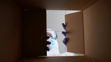 İspanyol hastanesinde kişisel koruyucu ekipman içinde bir kutu cerrahi maske paketleyen bir sağlık görevlisi. Karton kutunun içinden, eldivenli erkek hemşirenin resmine bak. Hastane Covid19