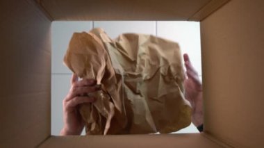 Bir siparişi korumak için karton bir kutunun içine kraft kağıdı koyan biri. Paketin içinden görüntüle.