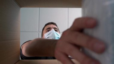 Karton bir kutuyu yeni maskelerle dolduran genç bir erkek hemşire. Karton kutunun içinden bak. Covid 19 'un sebep olduğu salgınla savaşmak için tıbbi malzeme..