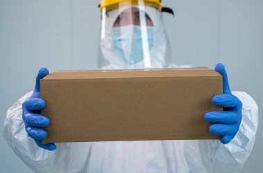 PPE 'si ve yüz kalkanı olan bir doktor içinde hijyenik malzeme olan bir kutu tutuyor. Sağlık görevlisine Coronavirus veya Cvid 19 hastaları için tıbbi malzeme verilir..