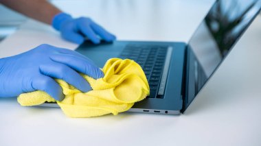 Eldiven giyen biri, koronavirüsü önlemek için dizüstünü temizler. Bir çalışma alanının dezenfeksiyon ve temizliği.