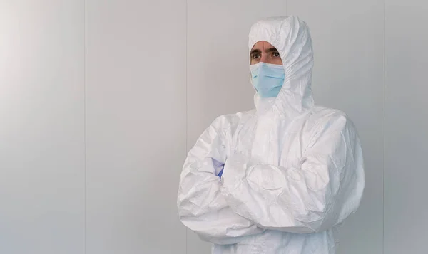 A health worker in a protective suit crosses his arms in the hospital during the pandemic caused by covid 19, coronavirus. The male nurse wears a surgical mask.