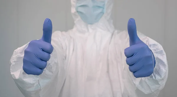 Close up of a nurse in a protective suit doing a thumbs up gesture with hands. Coronavirus pandemic, covid 19. Healthcare worker inside a hospital with PPE.