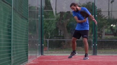 Seville, İspanya-03 Ağustos 2021: Padel oyuncusu duvara çarptıktan sonra topa vurmaya çalışıyor. Açık bir sahada raket tenis antrenmanı..