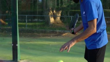 Seville, İspanya-28 Temmuz 2021: Ağır çekim topu sektiren ve açık hava sahasında servis yapan bir Padel oyuncusu.