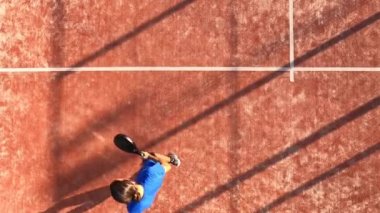 Açık havada raket oynayan bir adamın yukarıdan atışıyla topa vuruyor ve internete gidiyor..