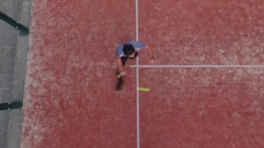 Açık hava sahasında maç yapan bir raket tenisçisinin yukarıdan görüntüsü.