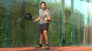 Sahada servis yapmak için topu sektiren ve raketle vuran bir Padel oyuncusunun yavaş hareketi..