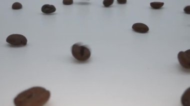 Beyaz arka plana düşen kavrulmuş kahve çekirdekleri yavaş çekimde..