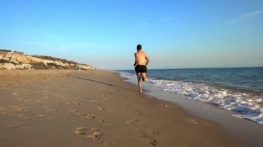 İspanyol plajında koşan sporcu. Yetişkin fitness adamı kısaca sahilde koşuyor. Güneşli bir sabahta denizde koşan yakışıklı, üstsüz adam.