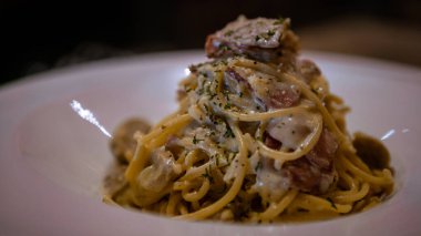 Restoranın masasında bir tabak spagetti alla carbonara. Pastırmalı, yumurtalı, krem soslu ve parmesan peynirli tipik İtalyan makarnası tarifi olan beyaz tabak. İtalya 'nın geleneksel mutfağı.