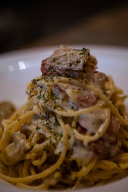 Restoranın masasında bir tabak spagetti alla carbonara. Pastırmalı, yumurtalı, krem soslu ve parmesan peynirli tipik İtalyan makarnası tarifi olan beyaz tabak. İtalya 'nın geleneksel mutfağı.