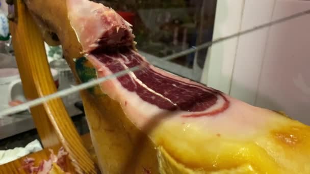 スペイン語でパタ ネグラとしても知られているセラノイベリアハムの前脚は 肉屋の切り身と木製のスタンドに取り付けられています — ストック動画