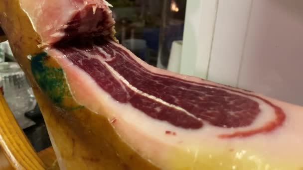 スペイン語でパタ ネグラとしても知られているセラノイベリアハムの前脚は 肉屋の切り身と木製のスタンドに取り付けられています — ストック動画