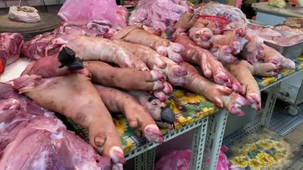台湾のファーマーズマーケットの肉屋のカウンターで豚の新鮮な生の足 アジアのストリートフード市場で売られているポークナックルの購入者 — ストック動画