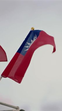 Tayvan bayrağının dikey ağır hareketi hafif bulutlara karşı zarafetle sallanarak barış ve gururu temsil ediyor. Barışçıl ve kültürel temalar için uygun.