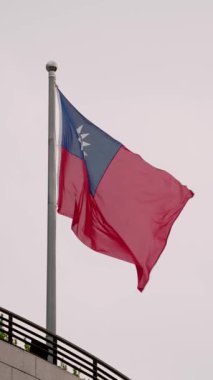 Çağdaş bir binanın tepesinde dalgalanan Tayvan bayrağının dikey yavaş hareketi birlik, gurur ve kentsel bir ortamda ilerlemeyi yansıtıyor..