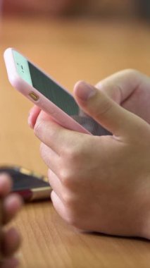 Closeup young students are reading a text on phone. Children looking smart phone screen over a wood desk in classroom. Teenager hand holding smartphone to search information. Education concept.