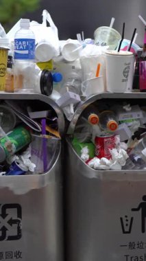 Taipei, Tayvan-13 Ağustos 2017: Taipei caddesindeki aşırı dolu çöp tenekesinden dökülen çöp. Asyalı bir kadın yolda yürürken çöp kutusuna çöp atıyor. Şişeler, teneke kutular ve diğer çöp kutuları.