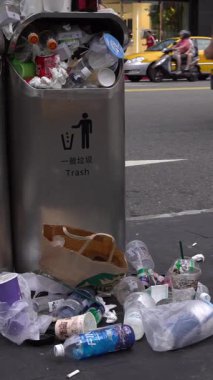 Taipei, Tayvan-13 Ağustos 2017: Taipei caddesindeki aşırı dolu çöp tenekesinden dökülen çöp. Asyalı bir kadın yolda yürürken çöp kutusuna çöp atıyor. Şişeler, teneke kutular ve diğer çöp kutuları.