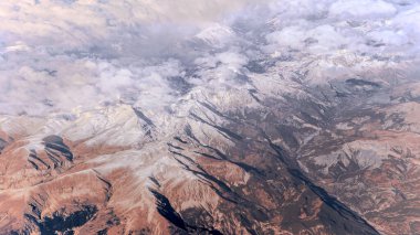 Tepelerin üzerinde bulutlar, engebeli dağ zirveleri ile kaplı Alpler manzarayı kaplıyor. Yüksek rakımlar hafif kar tozlarıyla kaplı, dağlara buzlu bir görünüm kazandırıyor.