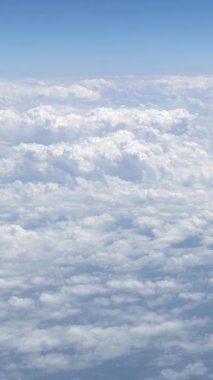 Gökyüzü açık mavi bulutlu harika bir manzara. Beyaz bulutların üzerinde bir uçağın penceresinden görülebilen güzel bir manzara. Uçaktan manzara.