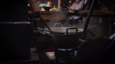 Japonya 'nın Fukuoka şehrinde geceleri sıcak ışıklar altında yemek yiyen ve rahat bir sokak yemeği atmosferi yaratan yatai yemek tezgahlarını gösteren yavaş çekim.