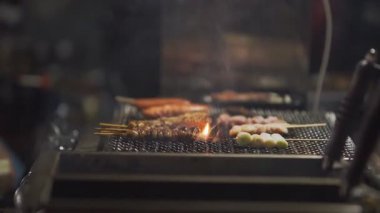 Japonya 'nın Fukuoka kentindeki bir yatai barbeküsünde et ızgara yaparken ağır çekim gösteriliyor. Parlayan közler, duman ve sıcak tonlarda sokak yiyeceklerinin enerjisini vurguluyor.