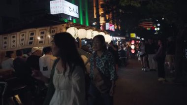 Fukuoka, Japonya-02 Ekim 2025: Japonya 'nın Fukuoka kentindeki, neon ışıklarıyla aydınlatılmış ve akşam yemeğinin keyfini çıkaran yerel halkla dolu yatai yiyecek tezgahlarıyla dolu işlek bir caddeyi yavaş çekim yakalamak