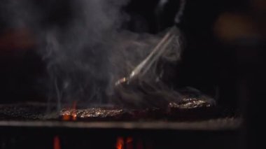 Japonya 'nın Fukuoka kentindeki bir yatai lokantasında sıcak bir ızgara tabakasından yükselen turuncu alevlerin ve dumanın yavaş çekim görüntüsü, sıcak yansımaları ve sokak yemekleri atmosferiyle birlikte.