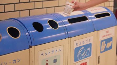 Fukuoka, Japonya-04 Ekim 2025: Düzenli bir kamu alanında, temiz alışkanlıklar, sürdürülebilirlik idealleri ve sorumluluk alanındaki mavi geri dönüşüm kutularına el sürme yavaşlaması