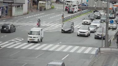 Fukuoka, Japonya-04 Ekim 2025: Yavaş çekim hava görüntüsü, Fukuoka, Japonya 'da Hakata İstasyonu yakınlarındaki büyük bir kavşakta açık ışık ve kentsel düzen içinde hareket eden araba ve otobüsleri gösteriyor