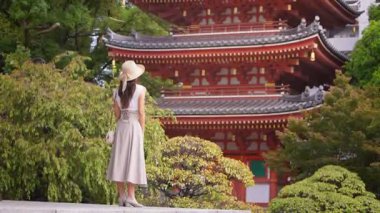 Bir kelebek geçerken, geleneksel bir Japon tapınağına hayran olan Asyalı bir kadının ağır çekimde görüntüsü. Mimarinin güzelliğinden büyülenmiş, hareketsiz duruyor..