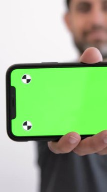 Beyaz arka plan stüdyosunun üzerinde yeşil ekranlı akıllı telefon gösteren beyaz bir adam. Elinde bir telefon cihazı olan kişi, bir reklam rengi kullanıyor.