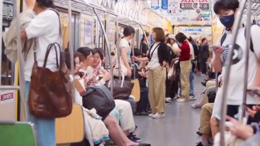 Fukuoka, Japonya-04 Ekim 2025: Kalabalık bir metro vagonunda kayışlar, insan yoğunluğu, nazik nüfuz, toplu taşıma alışkanlıkları ve çağdaş banliyö yaşam tarzı olan yavaş iç mekan yolcuları