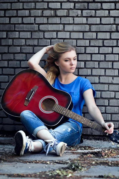 Porträt einer Frau mit einer Gitarre in der Nähe einer Ziegelmauer — Stockfoto