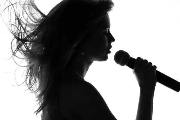 Silhouette di una donna che canta con un microfono in mano — Foto Stock