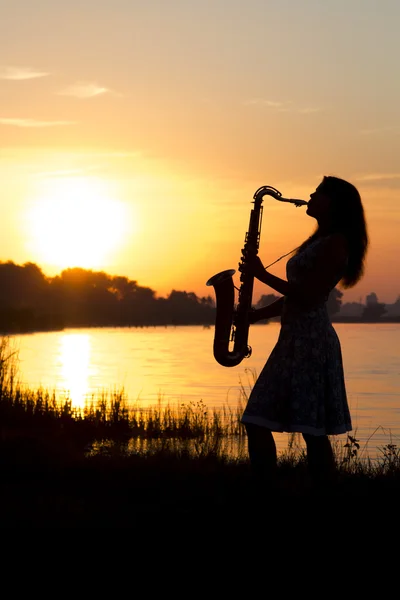 Silhouette einer jungen Frau, die im Morgengrauen auf dem Fluss ein Blasinstrument spielt — Stockfoto
